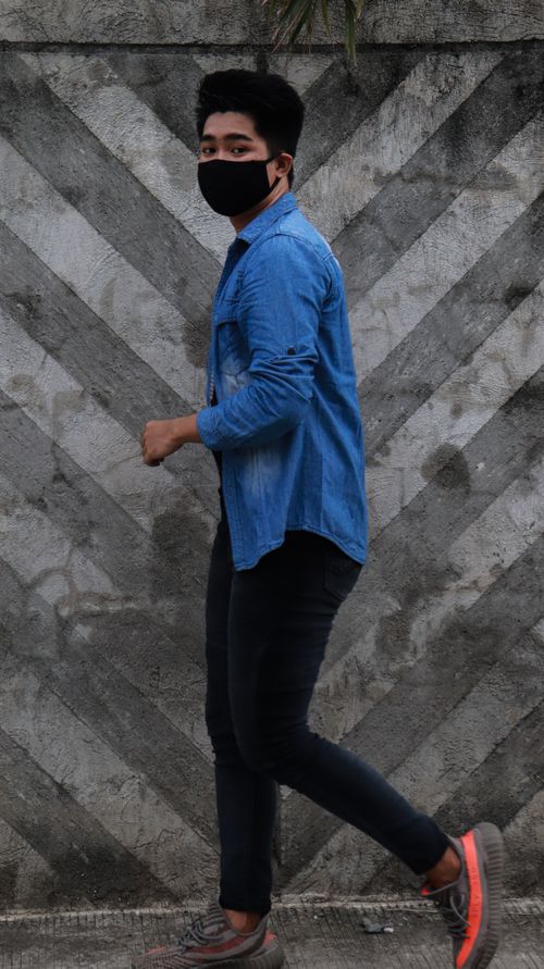 Free Asian man in denim shirt walking outdoors, wearing a face mask for safety. Stock Photo