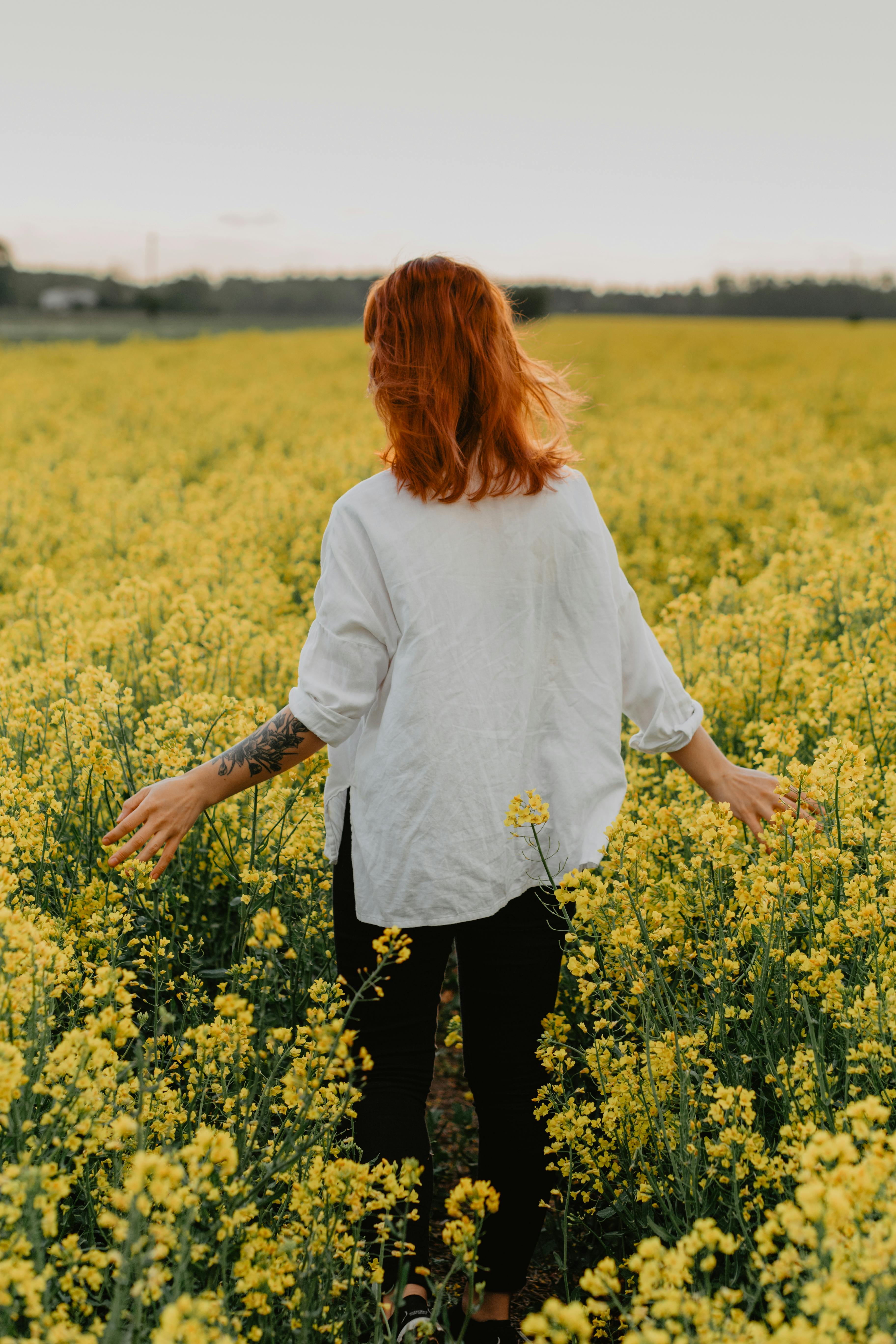 woman in white long sleeve shirt standing on yellow flower field