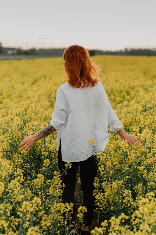 黄色い花畑に立っている白い長袖シャツの女性