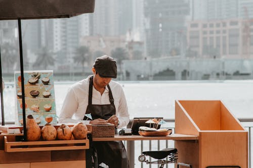 Man in White Dress Shirt and Black Apron Sitting in Front of Brown Wooden Table