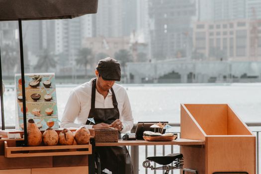 Street vendor selling food outdoors by the water with city skyline backdrop.