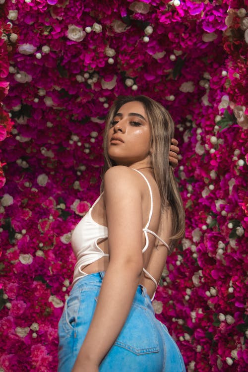 Woman in White Spaghetti Strap Top and Blue Denim Shorts Posing With Pink Flowers On Background