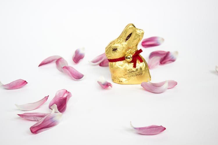 Golden Rabbit Figure On The White Surface Surrounded With Petals