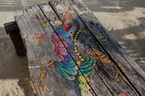 Free Artistic painting on a weathered wooden bench on a sandy beach, showcasing vibrant colors and creativity. Stock Photo