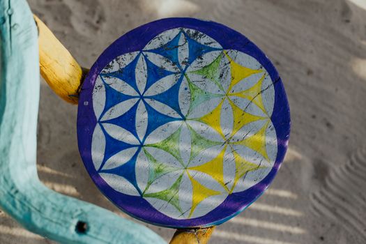 Colorful geometric pattern on a wooden stool against sandy beach backdrop.
