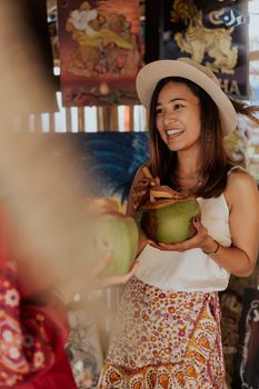 在热闹的市场里，一位年轻女子开心地捧着新鲜的椰子，散发出温暖开朗的气息