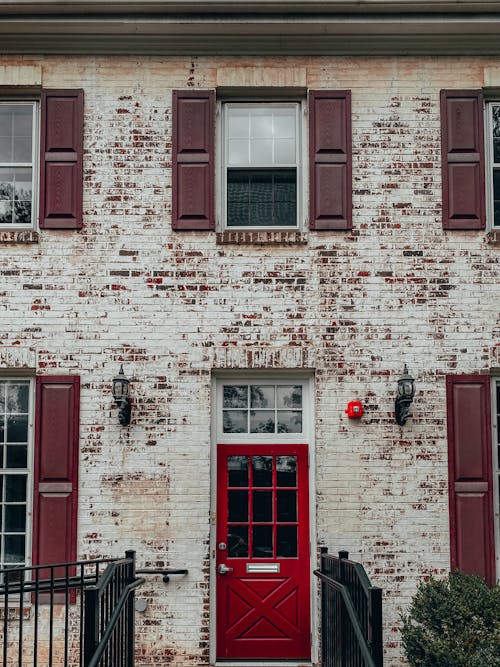 Free Exterior of old brick residential building with red door and windows with shutters in daytime Stock Photo