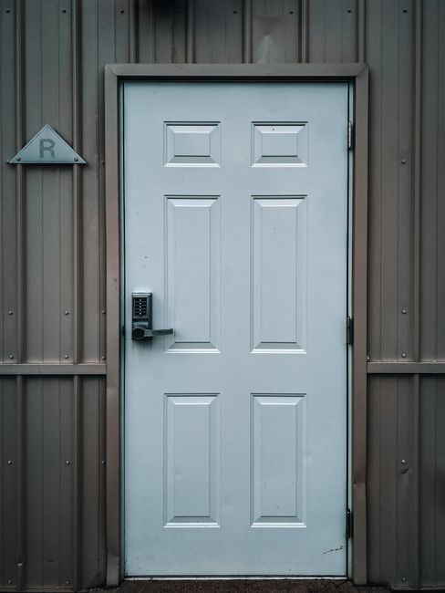 Closed white door with modern electronic lock placed in building with grey walls in daytime