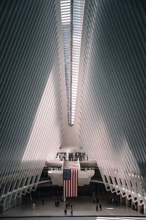 Interior of modern Oculus transportation hub at World Trade Center New York City Subway station with American flag hanging on center in sunny day