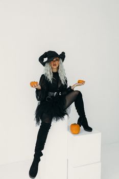 一个穿着女巫服装的时尚女人拿着南瓜，充满了完美的万圣节氛围