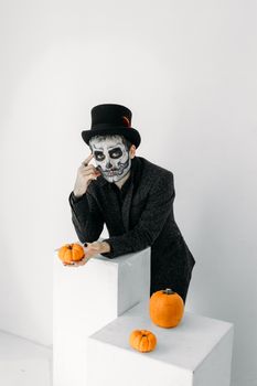 一个头骨妆容的男人在室内与南瓜摆姿势，体现了幽灵般的万圣节主题