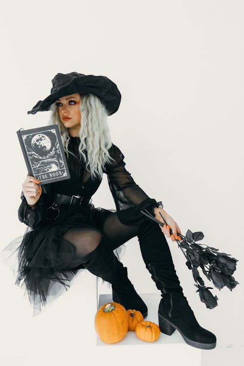 Free Woman in Black Witch Costume With A Book And Black Roses On Her Hands Stock Photo