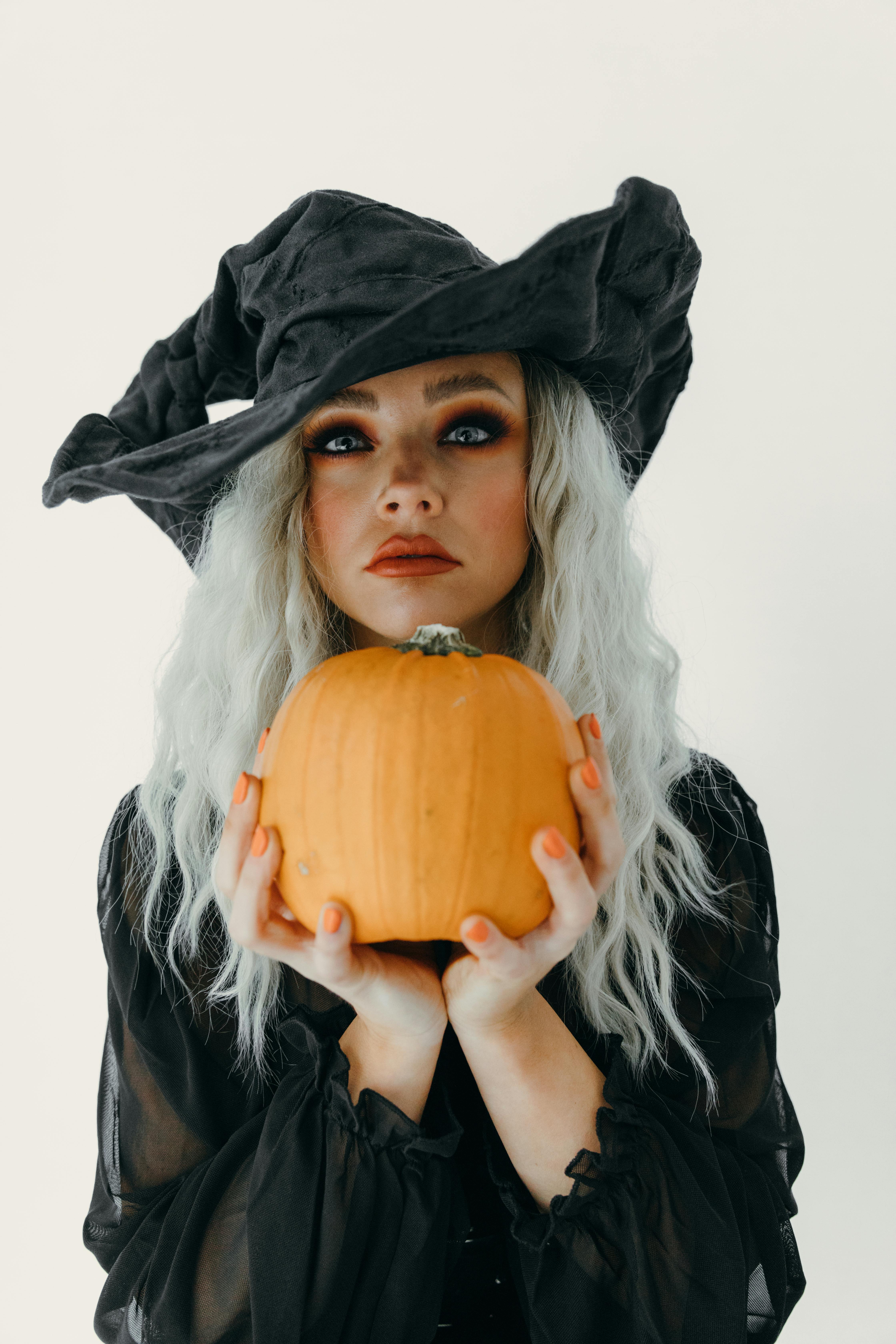 woman in a witch costume holding a big pumpkin