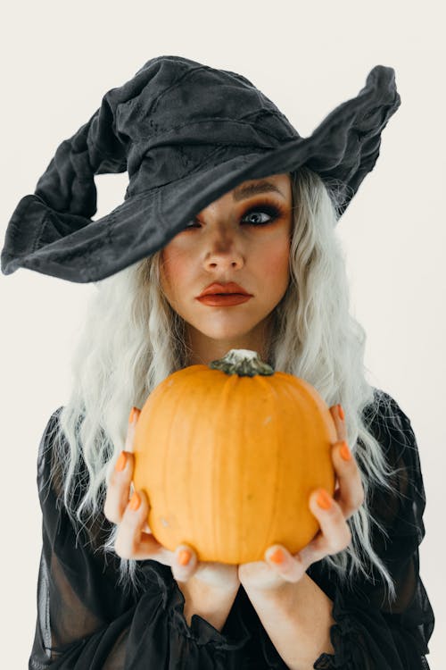 Woman in Black Witch Costume Holding Pumpkin