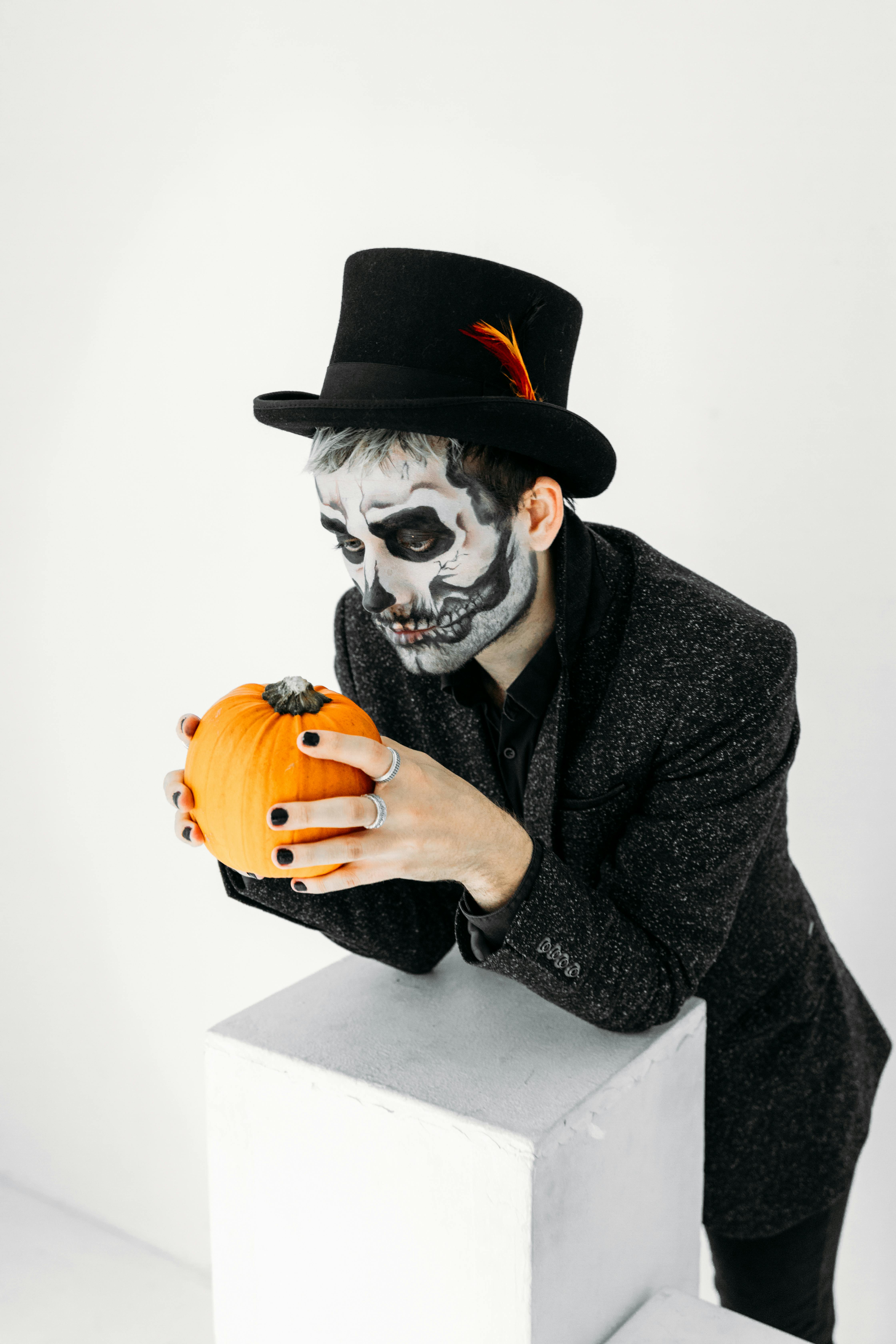 man with a scary face paint holding a pumpkin