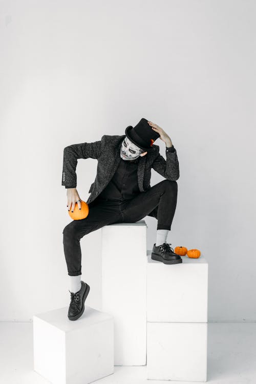 Man in Black Jacket and Black Pants Sitting on White Wall