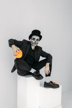 一个时髦的男人穿着怪异的万圣节服装，画着骷髅妆，手里拿着一个南瓜