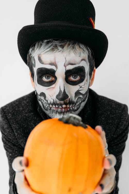 Free Person in Black and White Skull Face Paint Holding Pumpkin Stock Photo