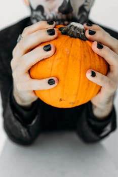 Eerie portrait of a person in skull makeup holding an orange pumpkin, perfect for Halloween themes.