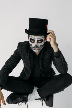 一个穿着黑色西装、画着头骨妆容的男人在室内摆出万圣节姿势
