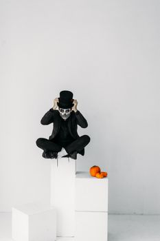 在艺术万圣节环境中，一位头骨化妆、戴着高顶礼帽的男人与南瓜合影
