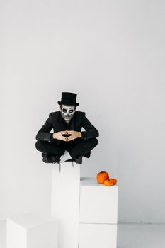 一张令人毛骨悚然的万圣节照片中，一个头戴高顶礼帽、脸上涂满油彩的男人坐在南瓜块上