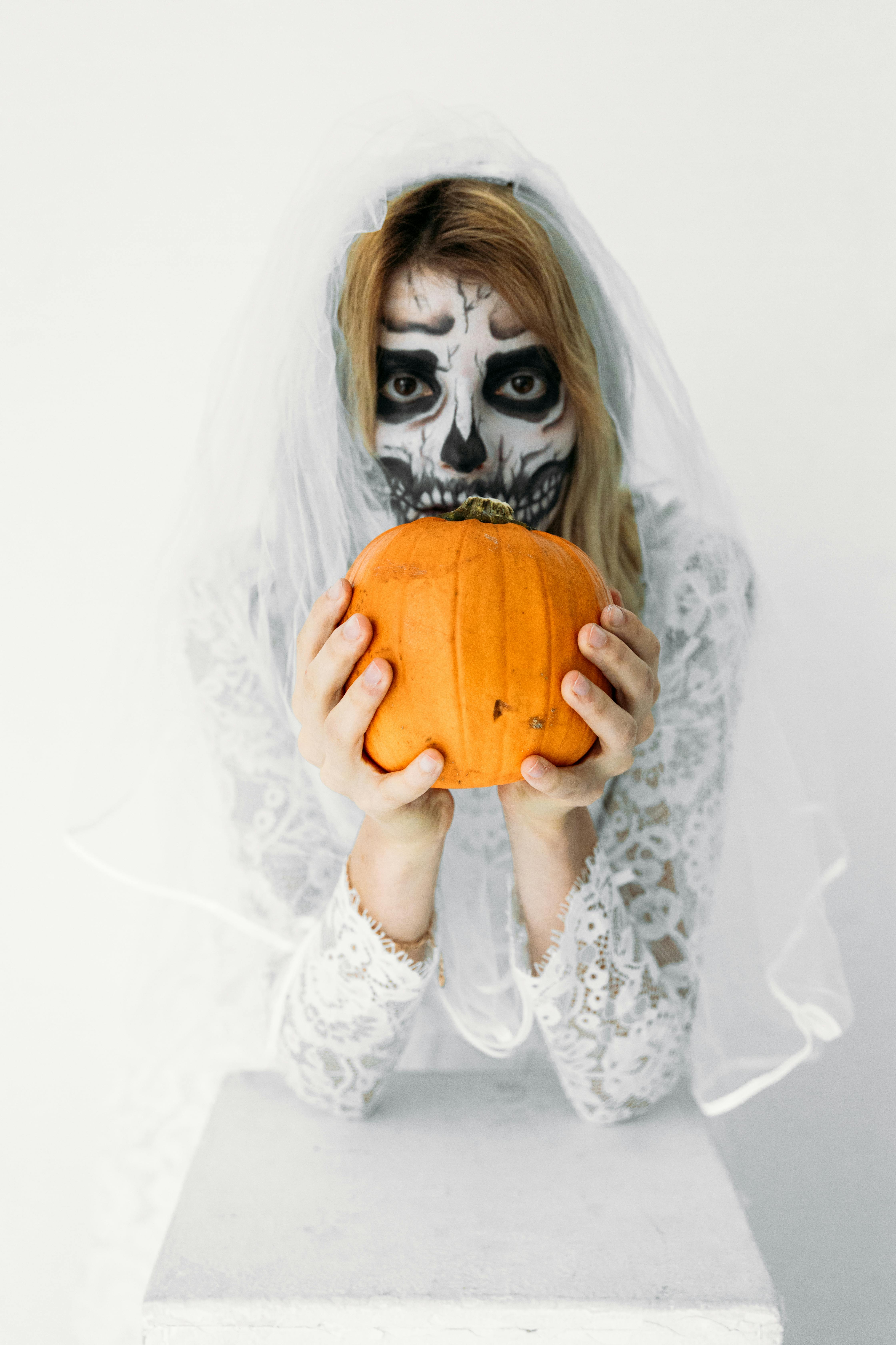 Free A woman in skull face paint holds a pumpkin, dressed as a spooky bride. Perfect for Halloween themes. Stock Photo