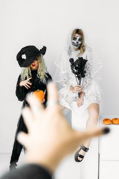 两名身着万圣节服饰、化着妆的女性在室内与南瓜合影，营造出一种怪异的氛围