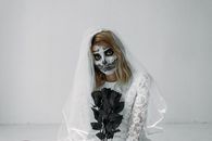 身着白色礼服、画着骷髅妆的新娘手持黑玫瑰，宛如幽灵，是完美的万圣节主题