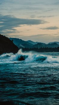 Majestic waves crash against Aceh's coastline, framed by distant mountain ranges under a moody sky.