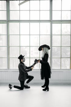 A creative Halloween marriage proposal featuring a couple in gothic attire with face paint in a bright room.