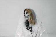 一位身着蕾丝婚纱、头戴面纱的女子，脸上画着骷髅妆容，手持一朵黑玫瑰，构成了一幅令人难忘的新娘肖像