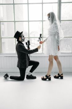 一个跪着的骷髅脸男人提议，在令人毛骨悚然的室内环境中为新娘献上黑玫瑰