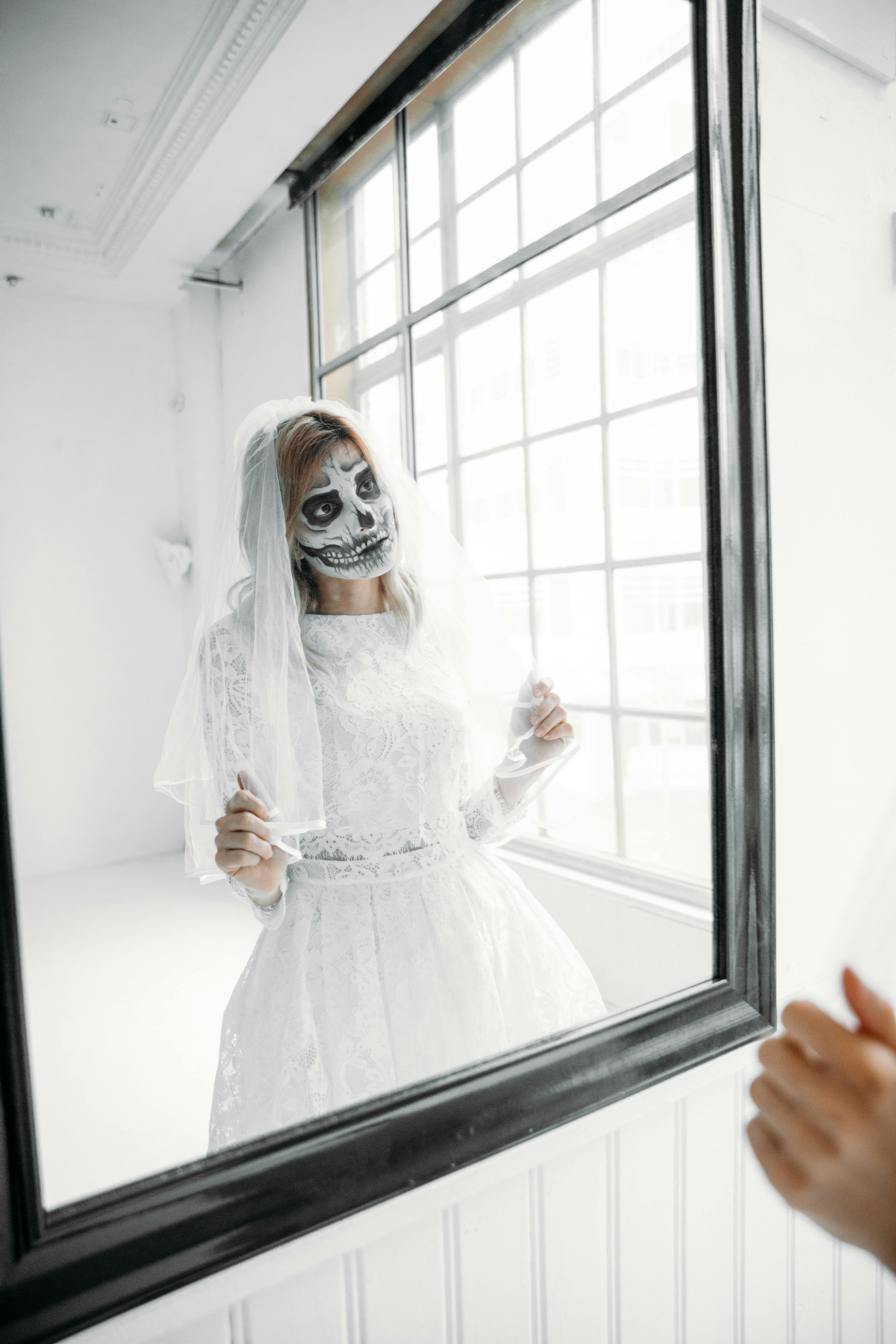 woman with face paint wearing a white veil and a white dress on a mirror