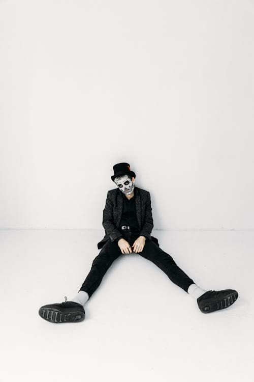 Man in Black Jacket and Black Pants Wearing Face Paint While Sitting on The Floor