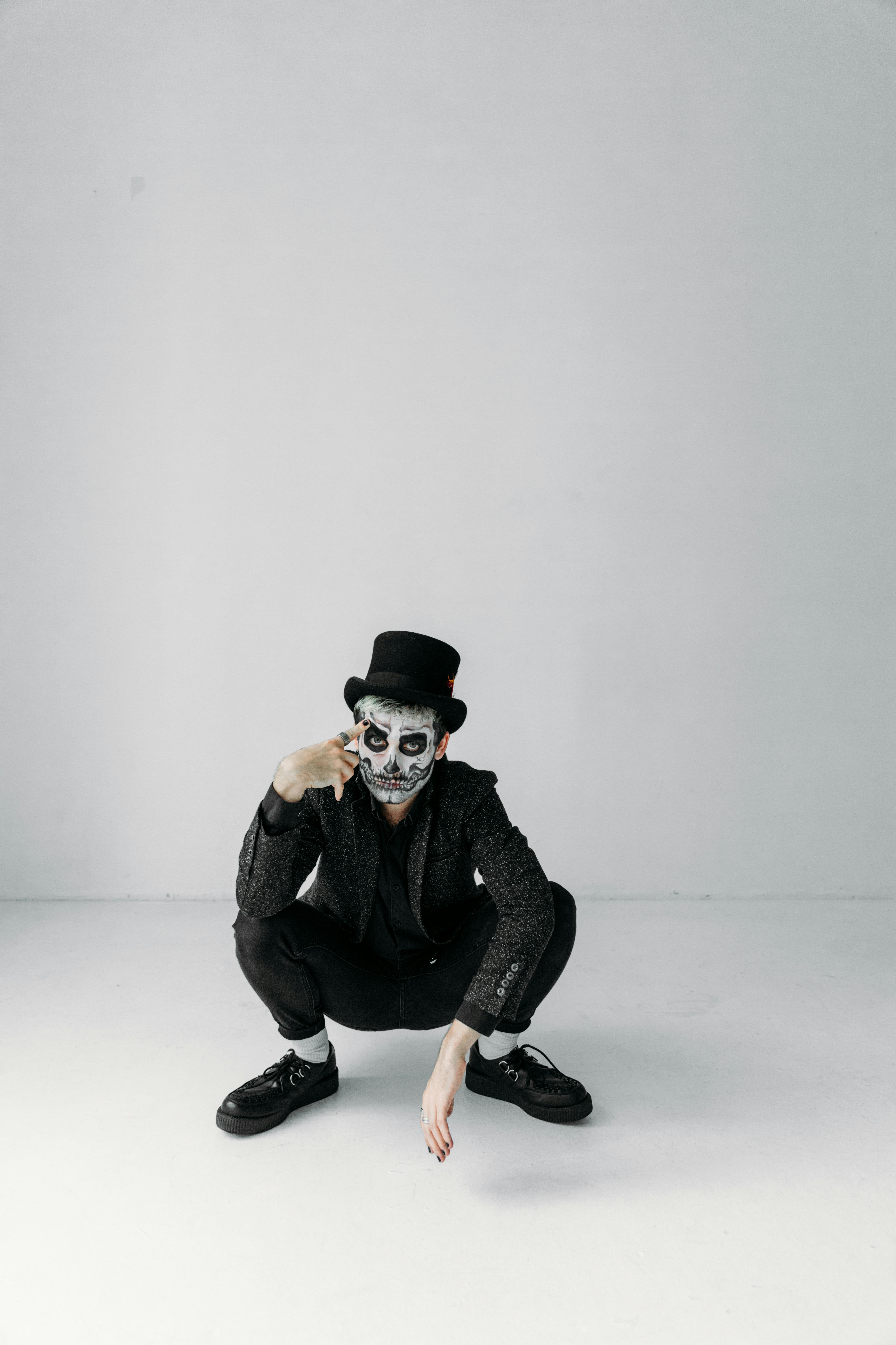 man in black jacket and black pants wearing black hat sitting on white floor