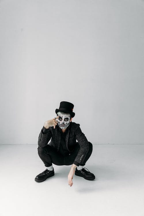 Man in Black Jacket and Black Pants Wearing Black Hat Sitting on White Floor