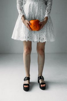 一位身着白色蕾丝连衣裙的女子拿着小南瓜，营造出万圣节主题