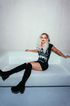 一位金发碧眼的时髦女人，穿着哥特风格的衣服，坐在室内的白色沙发上