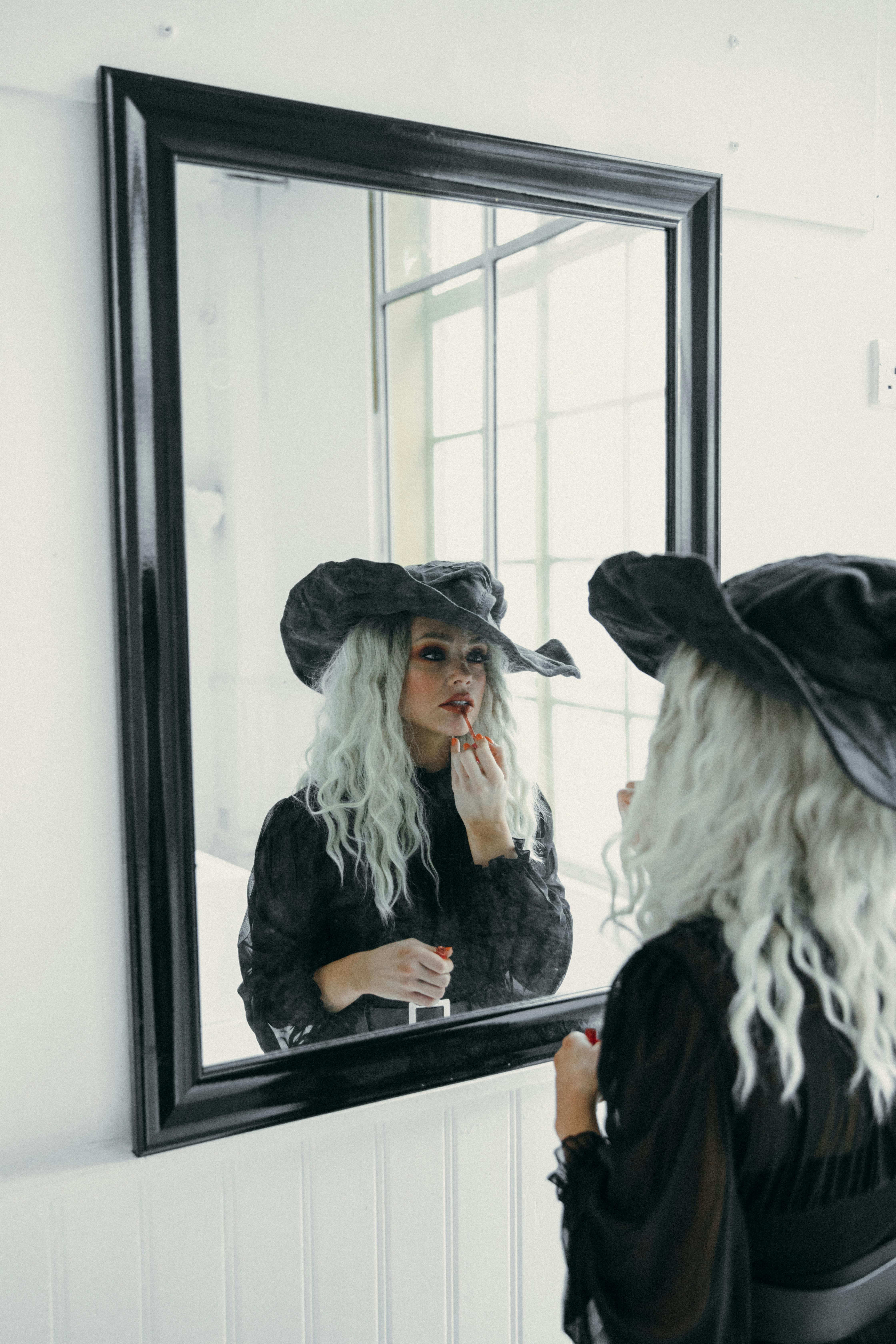 woman in black applying lipstick in front of a mirror