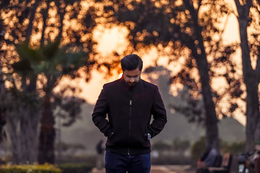 A man strolls in a park during a serene autumn sunset, reflecting tranquility.