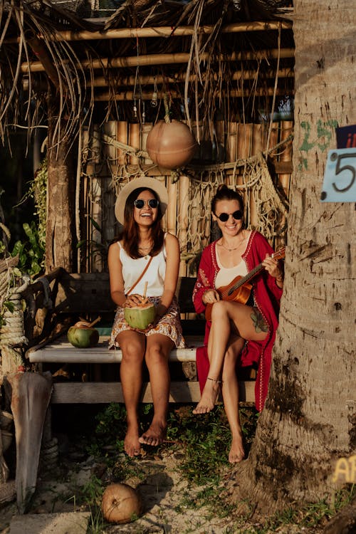 Free Women sitting on a Bamboo Bench while Playing Guitar and Drinking Coconut Juice Stock Photo