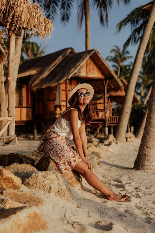 Woman in White and Brown Floral Dress Sitting on A Rock