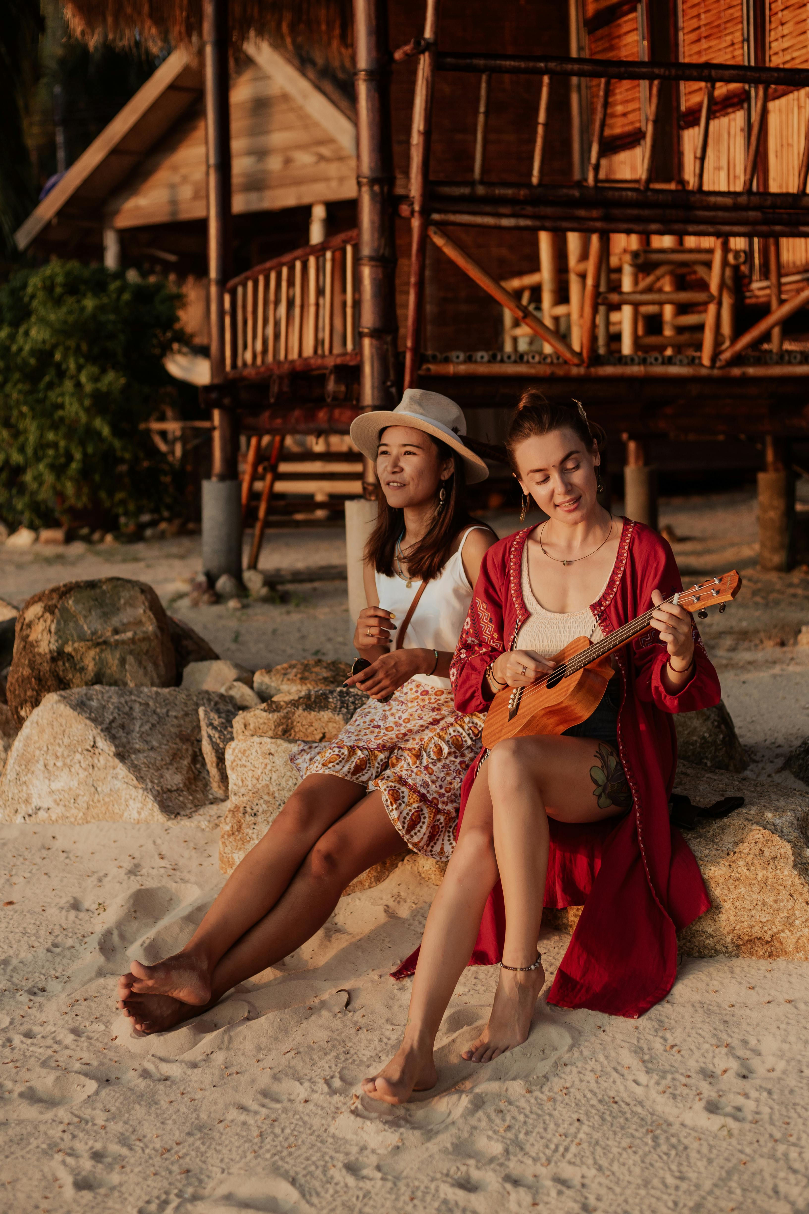 woman playing ukulele sitting beside woman on rock