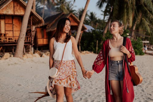 Free Women Holding Hands While Walking on White Sand  Stock Photo