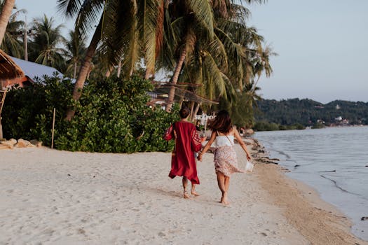 Two women holding hands and walking along a sandy tropical beach, enjoying their summer vacation.