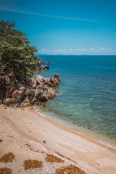 A serene Thai beach with turquoise waters and rocky coastline under a blue sky, perfect for a tropical getaway.