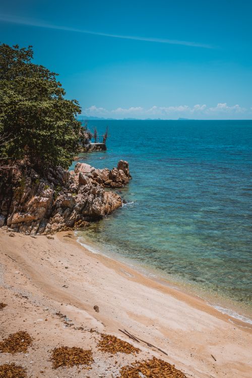 Free A serene Thai beach with turquoise waters and rocky coastline under a blue sky, perfect for a tropical getaway. Stock Photo
