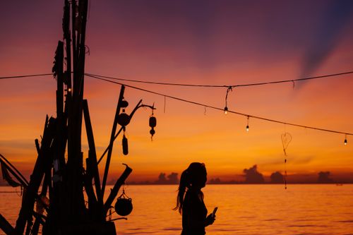 Free Silhouette of a woman enjoying the serene sunset at the beach with string lights and a warm, colorful sky. Stock Photo