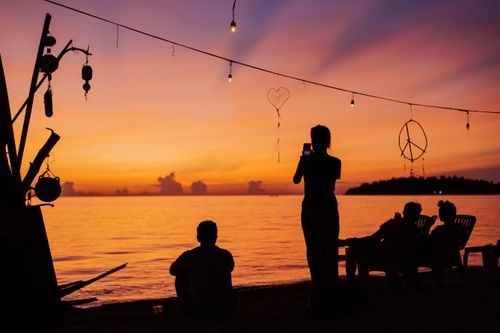 Free A beautiful beach scene with silhouettes at sunset, featuring hanging lights and a tranquil ocean view. Stock Photo